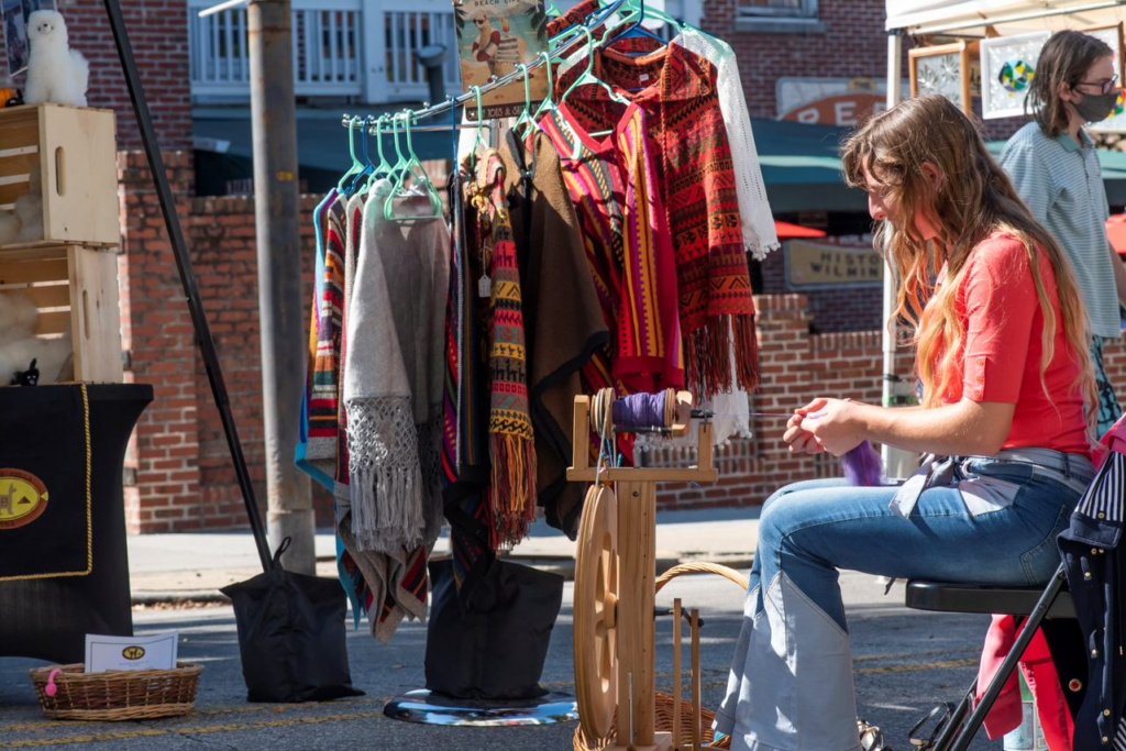 Woman sitting near a clothing rack, outside. Thift shops to check out in Wilmington, NC. Wilmington Vacation Homes